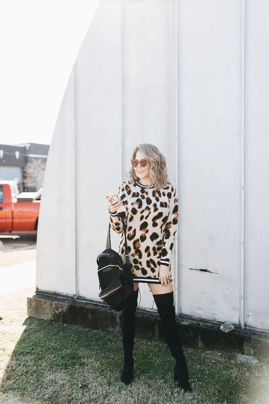 Looking for TRENDY Valentine's Day outfit ideas? Style Blogger Life Lutzurious styles this ADORABLE leopard dress with black OTK boots and the cutest red heart-shaped sunnies you ever did see.